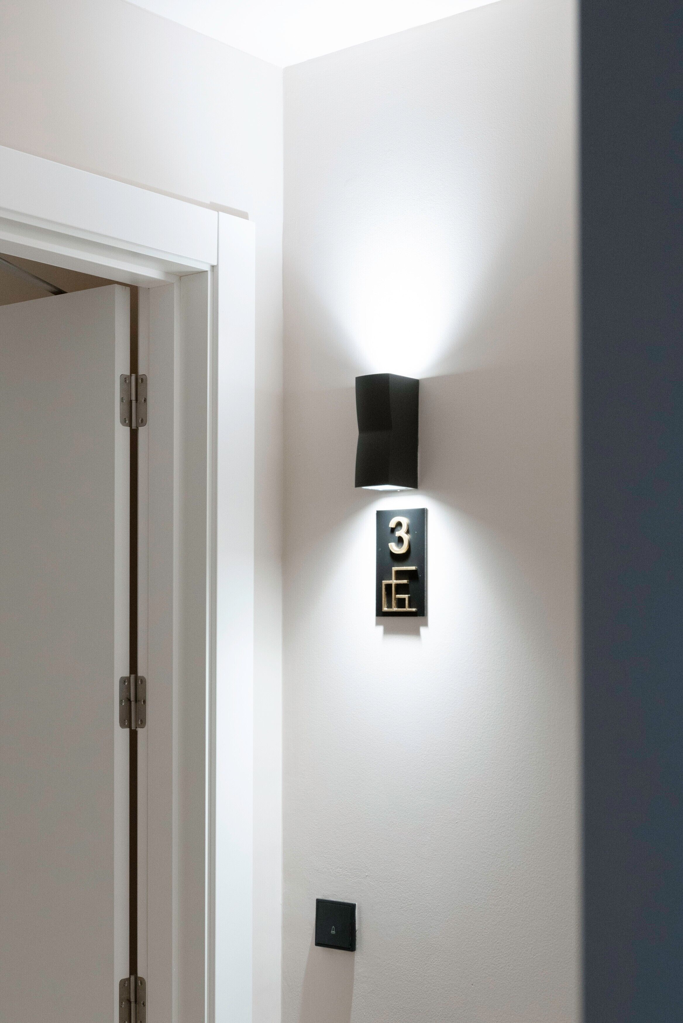 Un pasillo con una puerta, un aplique en la pared y una placa con el número 3.