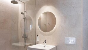 Un baño moderno con ducha envuelta en vidrio, un espejo redondo, un lavamanos blanco y un inodoro.