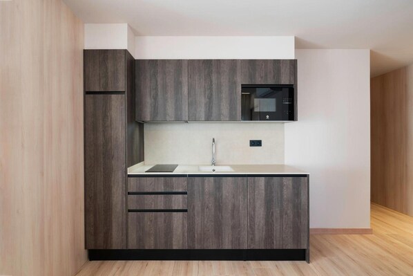 Una cocina moderna con armarios de madera oscura, encimera blanca y microondas empotrado.