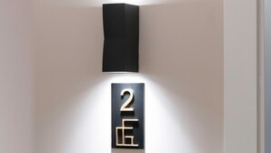 Una lámpara de pared con un portalámparas negro y un letrero con números negro y dorado.