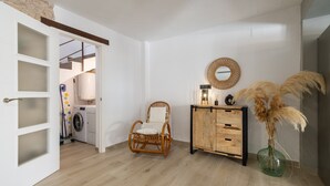 A room with a washing machine, a wicker chair, a wooden cabinet, and a vase with pampas grass. - Apartment in Deltebre Casa Fotostudi37 (Deltebre)
