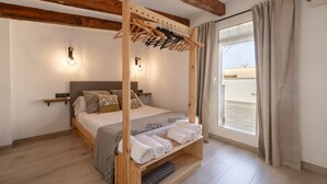 A bedroom with a wooden bed frame, a built-in shelf with towels, a hanging clothes rack, and a window with curtains. - Apartment in Deltebre Casa Fotostudi37 (Deltebre)