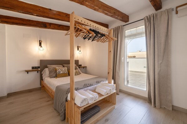 A bedroom with a wooden bed frame, a built-in shelf with towels, a hanging clothes rack, and a window with curtains.