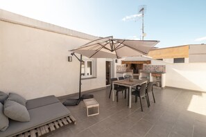 A rooftop patio with a dining table, chairs, a sofa, and a large umbrella.