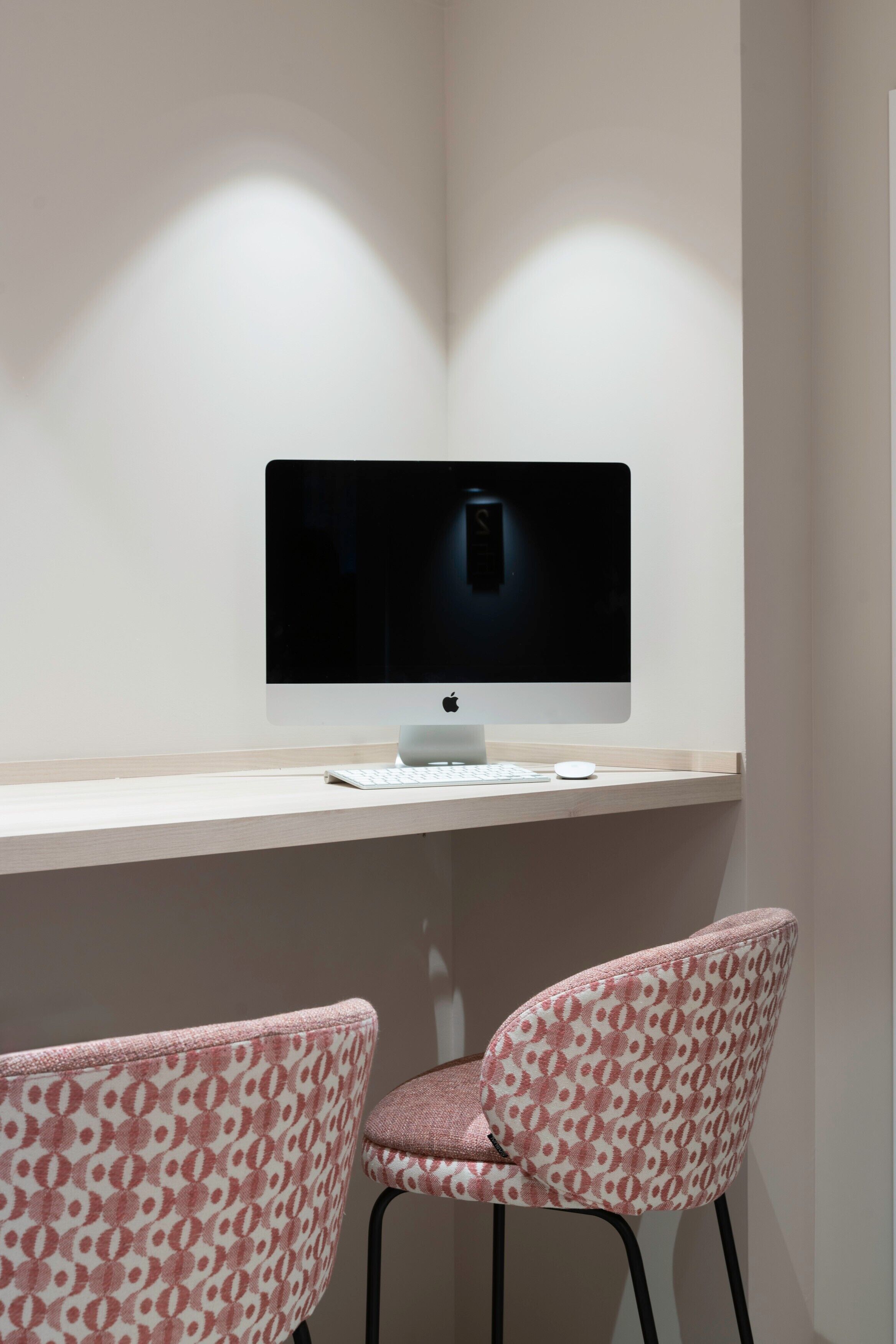Habitación minimalista con escritorio, monitor de computadora y dos sillones con estampado.