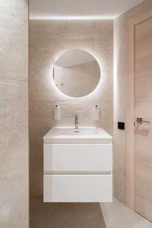 Une salle de bain moderne avec un meuble-lavabo blanc, un miroir rond et une porte en bois.
