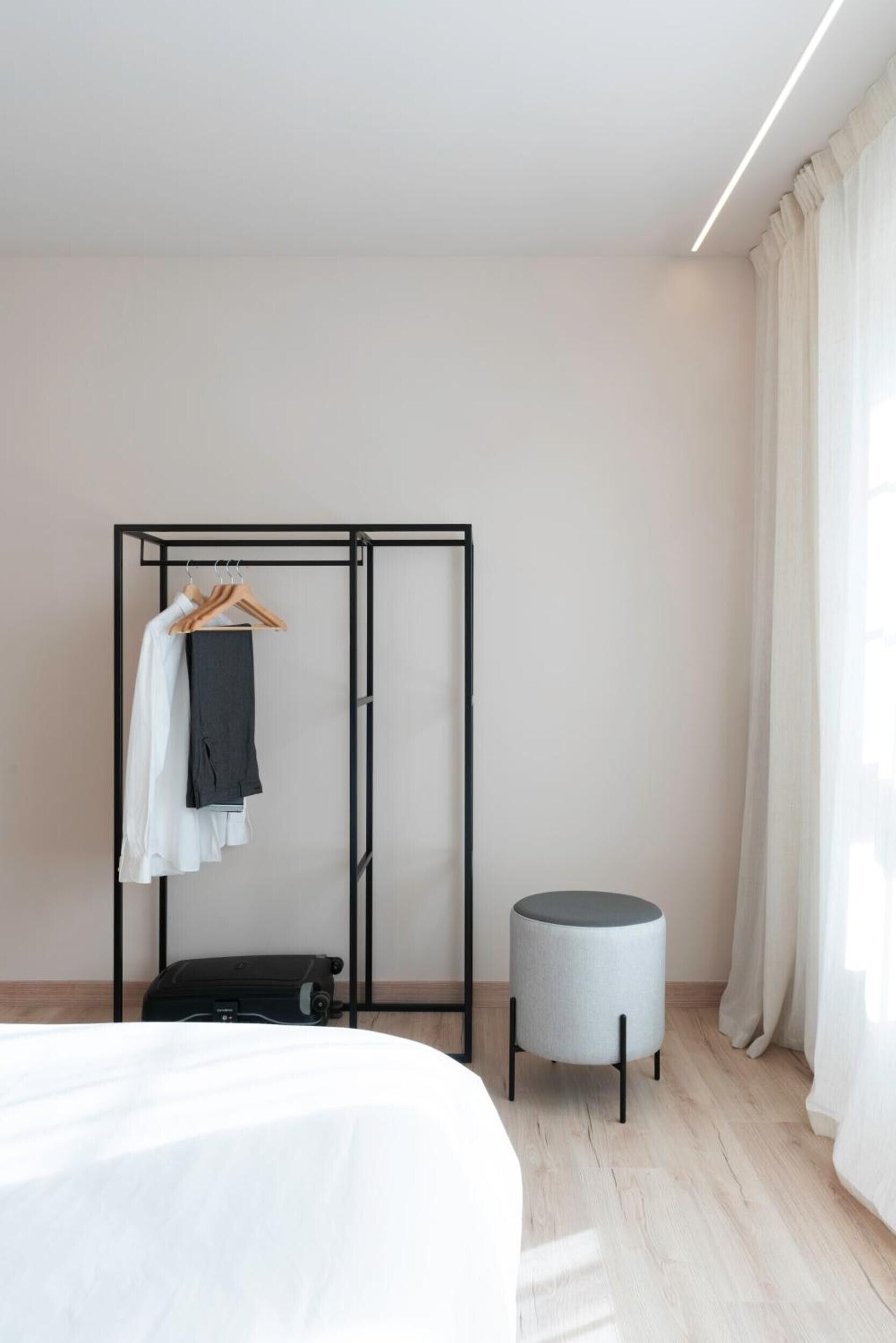 Een hotelkamer met een bed, een kledingkast, een rond krukje en een koffer.