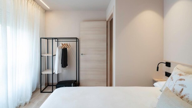 Habitación de hotel con cama, armario, espejo, mesita de noche y ventana con cortinas.