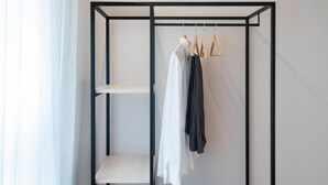 Una habitación con un armario metálico negro, una maleta y ropa colgada.