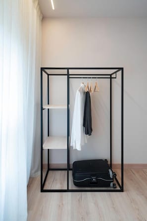A room with a black metal wardrobe, a suitcase, and hanging clothes.