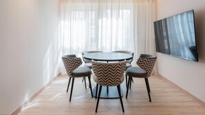 Un comedor moderno con una mesa redonda y seis sillas, un ventanal con cortinas translúcidas y un televisor de pantalla plana montado en la pared.