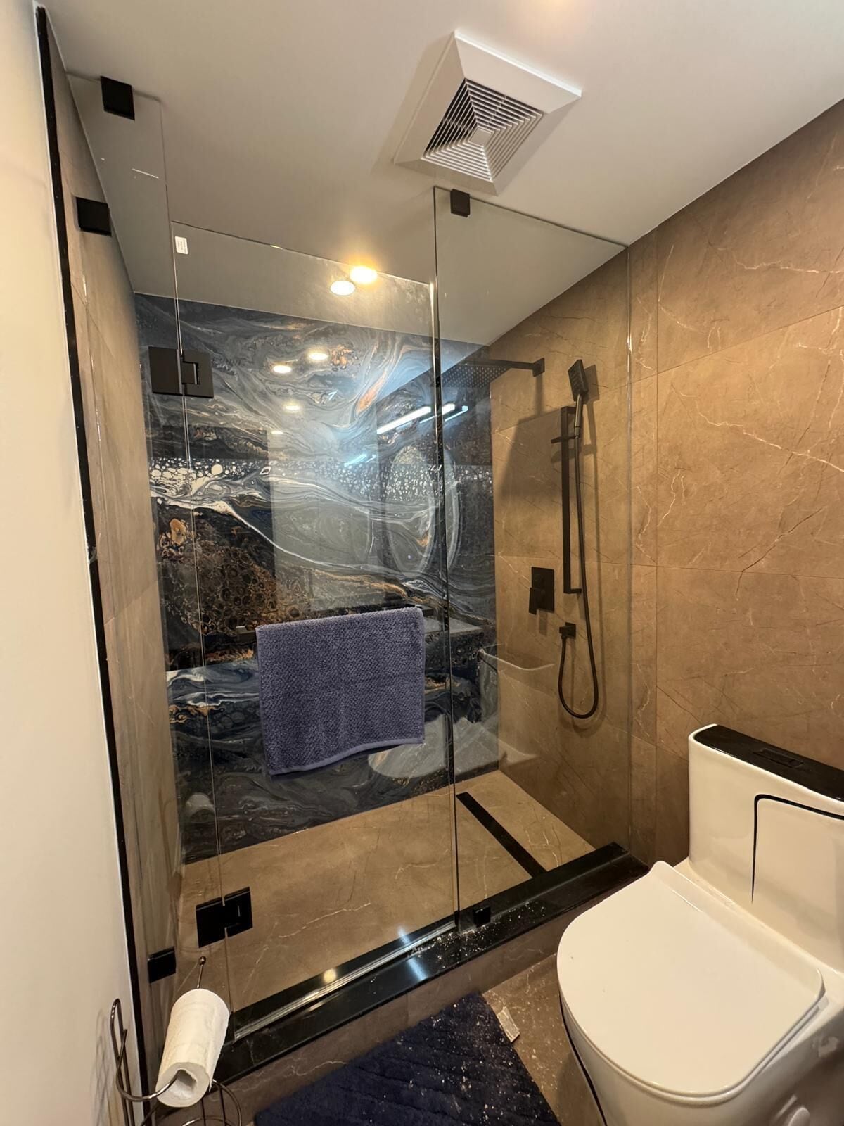 Une salle de bain moderne avec une douche à parois de verre, des murs en marbre et des toilettes blanches.