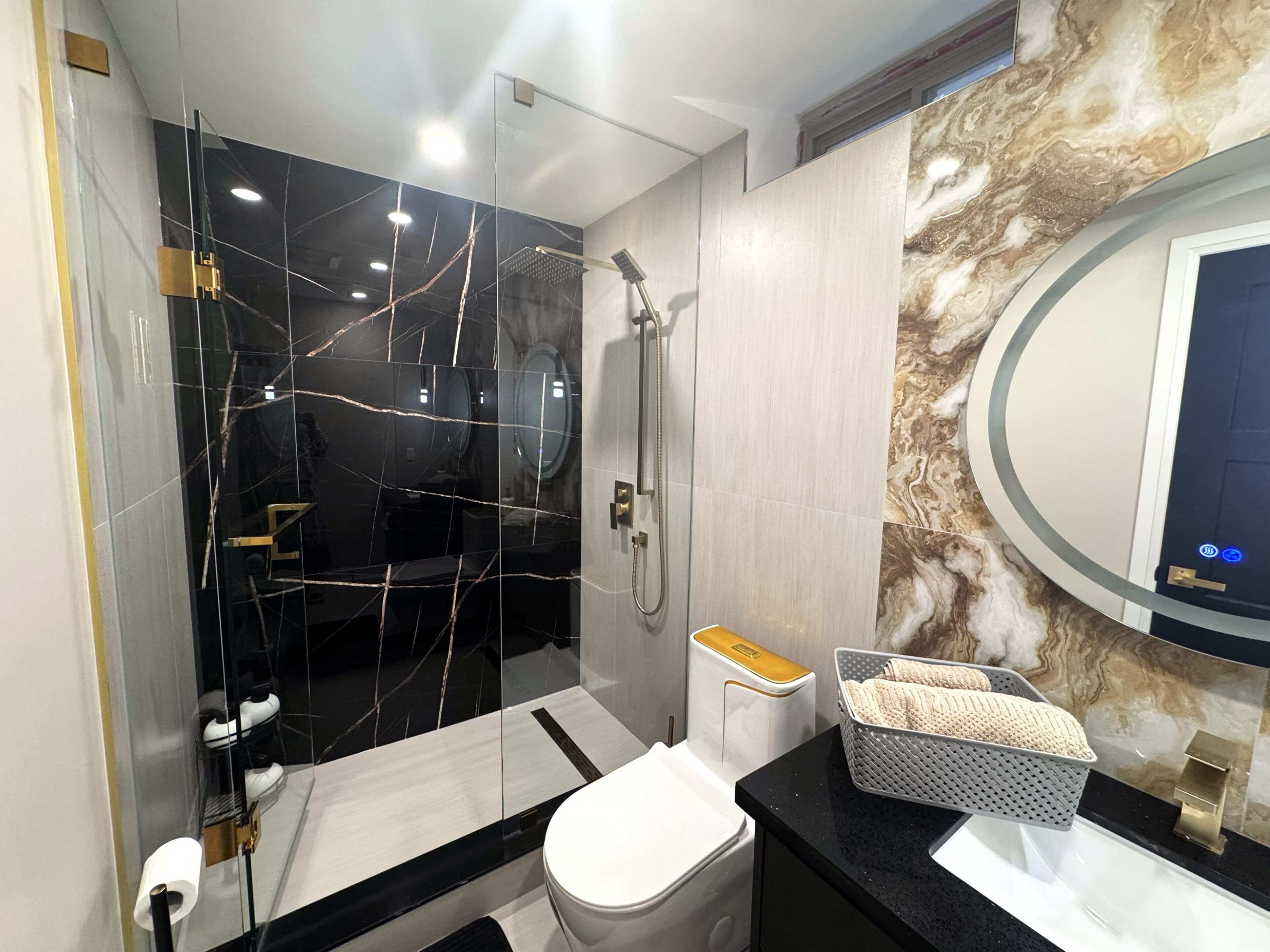 A modern bathroom with a glass-enclosed shower, a toilet, and a vanity with a marble backsplash.