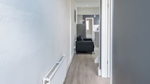 Un pasillo estrecho con un radiador a la izquierda, un sofá de color oscuro en el centro y una puerta que da a otra habitación.