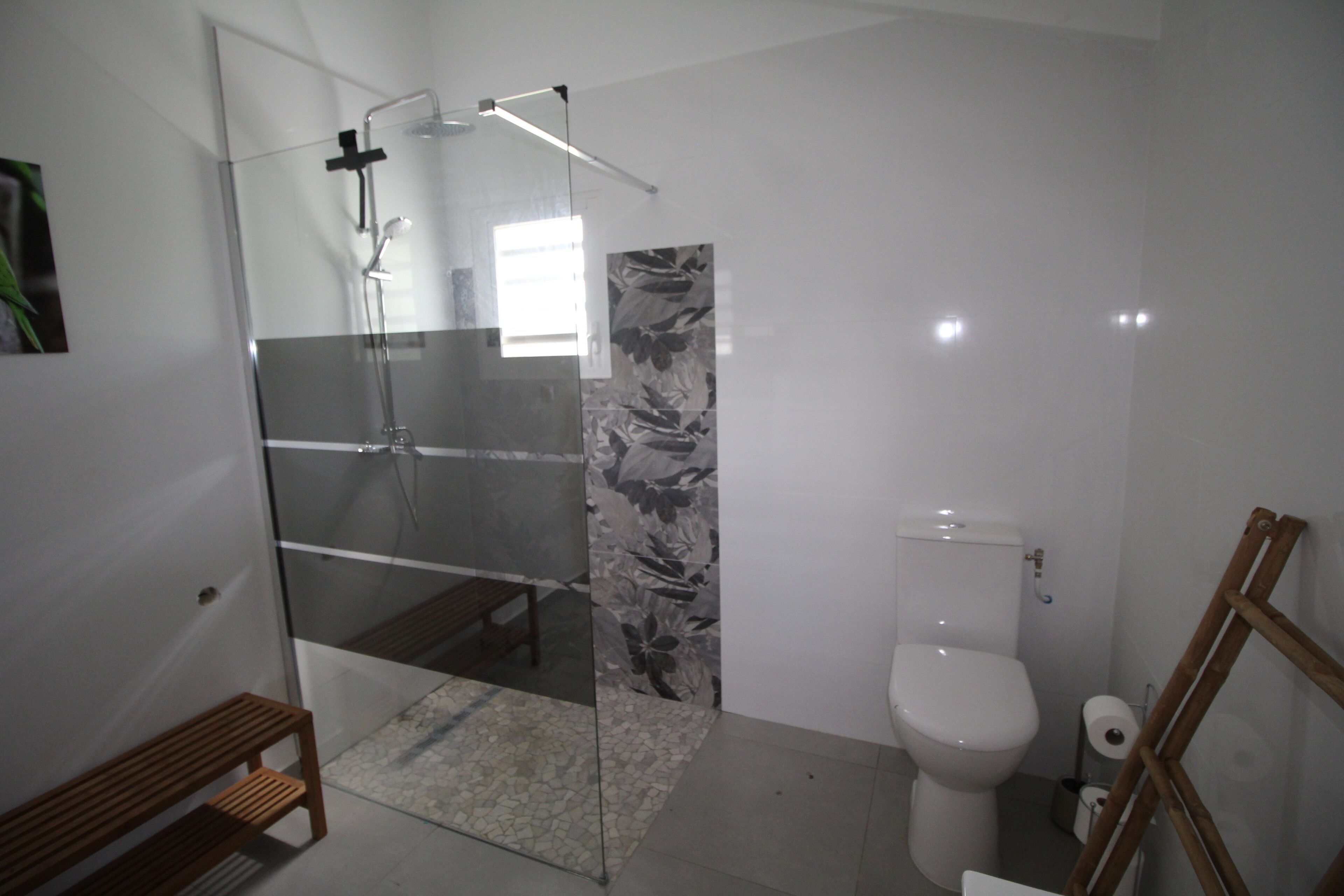 Ein modernes Badezimmer mit Duschkabine aus Glas, Toilette und einer hölzernen Sitzbank.