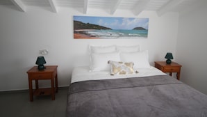Un dormitorio con cama, dos mesitas de noche, un cuadro de una playa y un techo con vigas de madera.