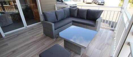 A covered patio with a grey sectional sofa, a glass-top coffee table, and a matching ottoman.