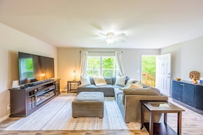 A living room with a TV, sofa, ottoman, and a ceiling fan. - Private Riverfront home w/ Hot tub, central to ONP (Beaver)