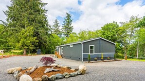 A single-story cabin with a gravel driveway, surrounded by trees and a small garden with rocks and plants. - Private Riverfront home w/ Hot tub, central to ONP (Beaver)
