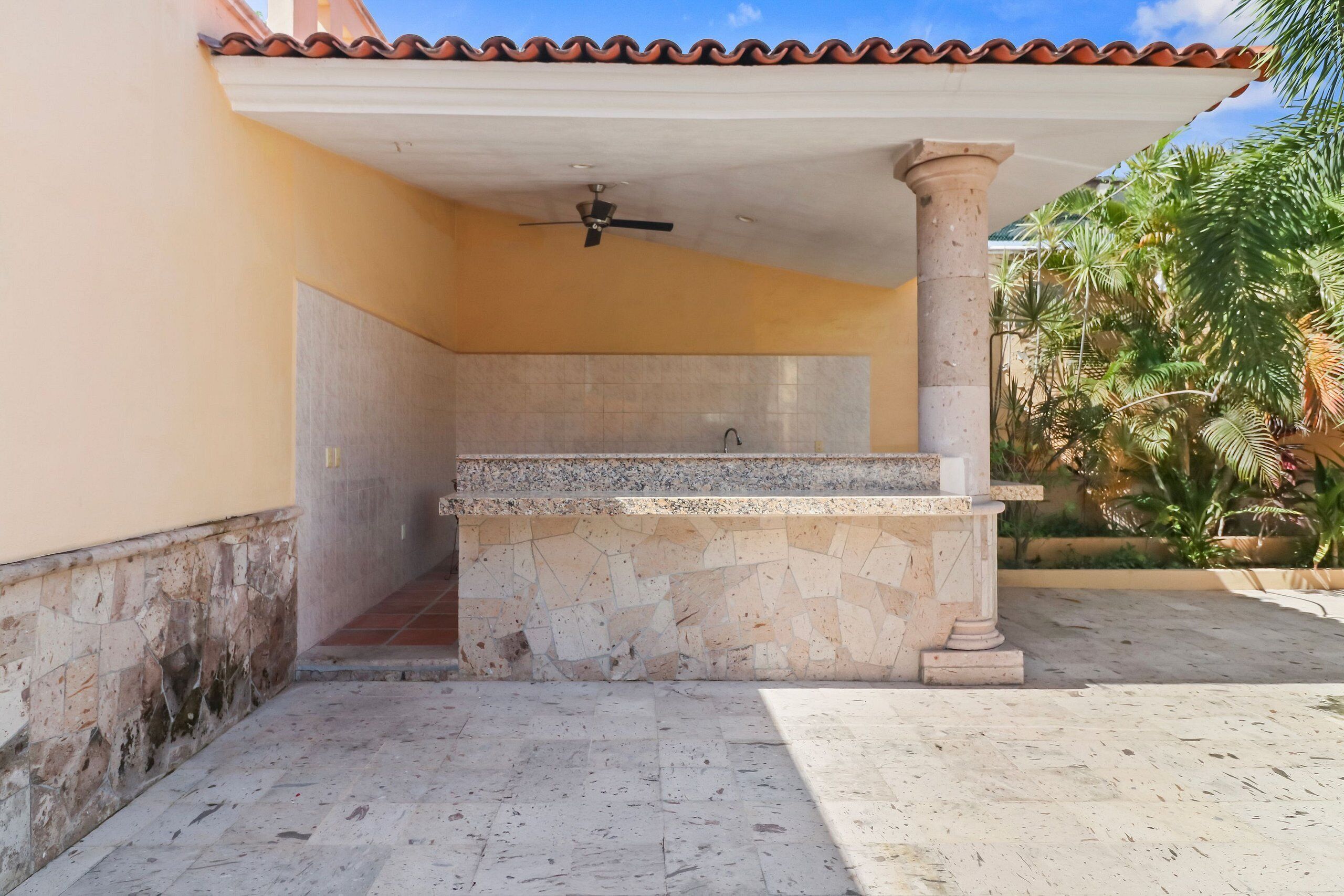 An outdoor patio with a stone bench, a ceiling fan, and a column.