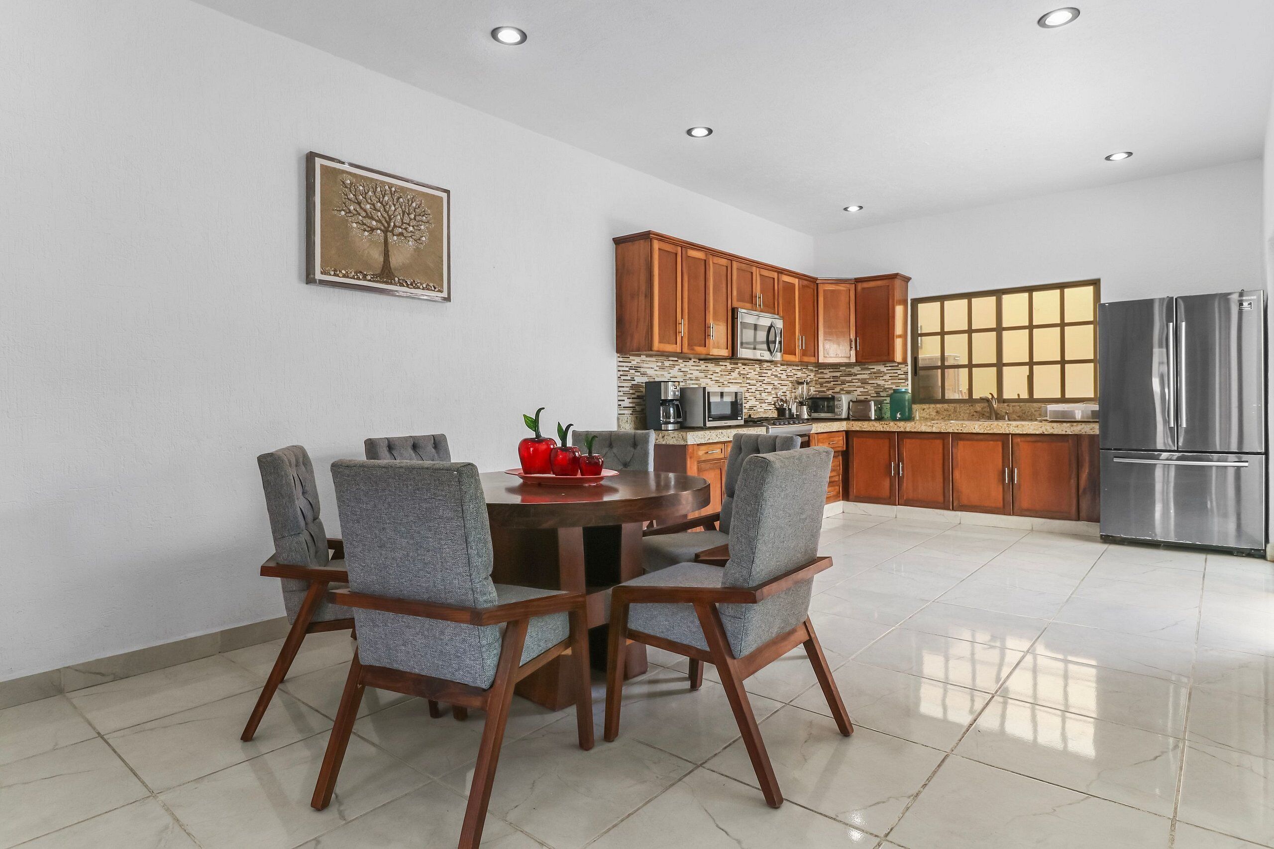 A modern kitchen with wooden cabinets, a stainless steel refrigerator, and a dining area with a round table and chairs.