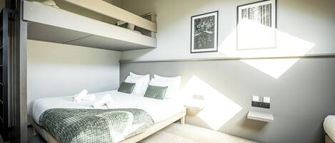 Une chambre avec un lit superposé, un lit avec des oreillers, une table de chevet et deux tableaux encadrés accrochés au mur.