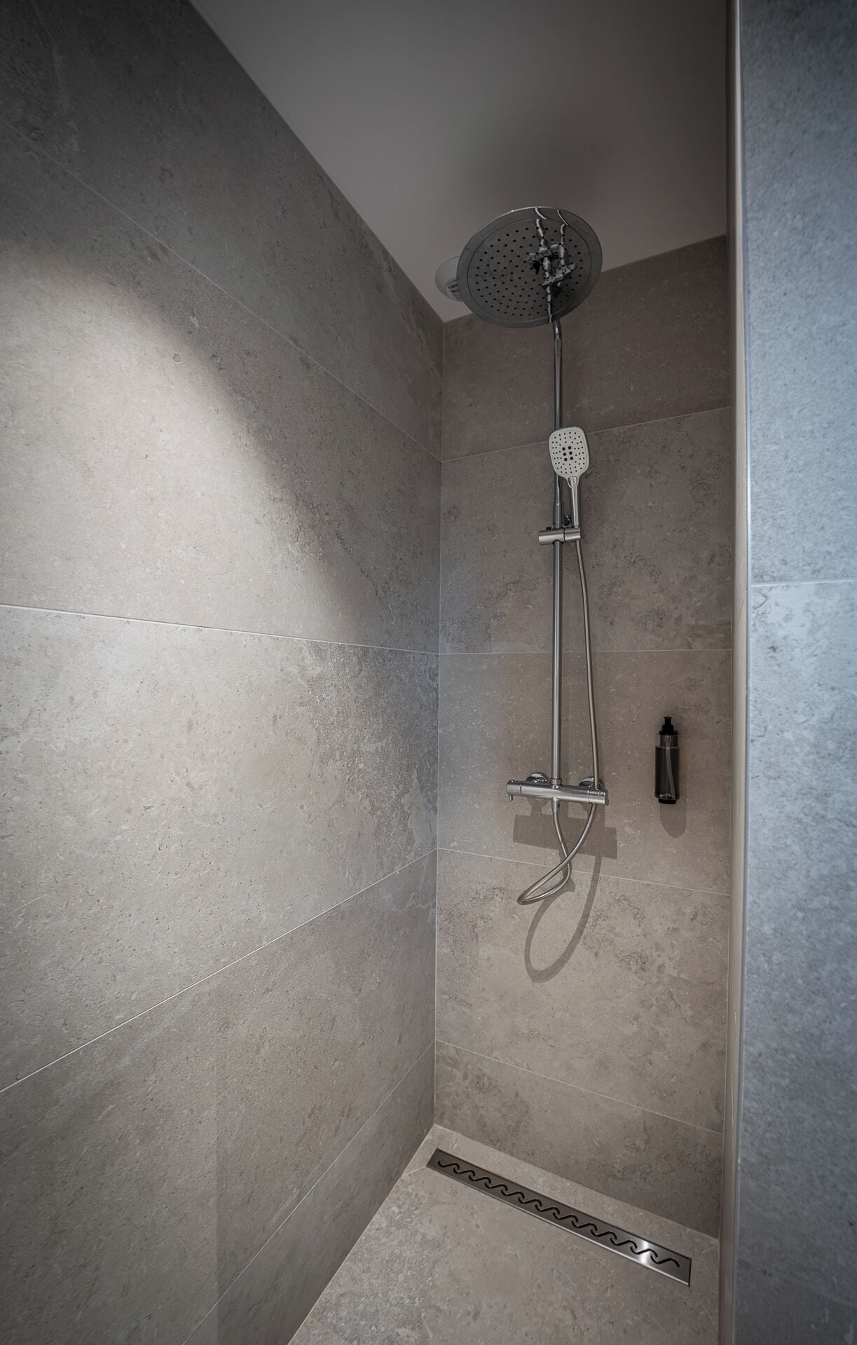 Une douche équipée d’un pommeau de douche à main, d’un panneau de commande fixé au mur et d’un drain.