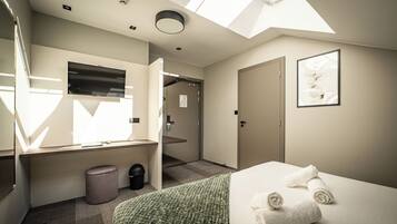 Una habitación de hotel moderna con tragaluz, cama con toallas, cubo de basura y puerta que da a otra habitación.
