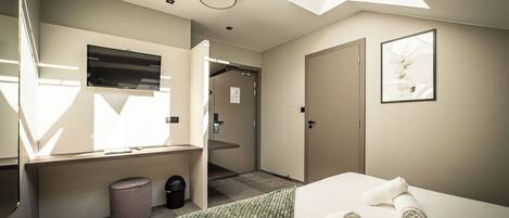 A modern hotel room with a skylight, a bed with towels, a trash bin, and a door leading to another room.