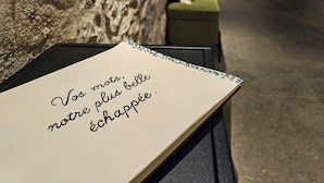 A room with a stone wall, a green sofa, and a table with a note. - L'Echappée Vosgienne (Gérardmer)