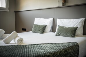 Ein ordentlich bezogenes Bett mit weißen und grünen Kissen, einem aufgerollten weißen Handtuch und einer grünen Decke.