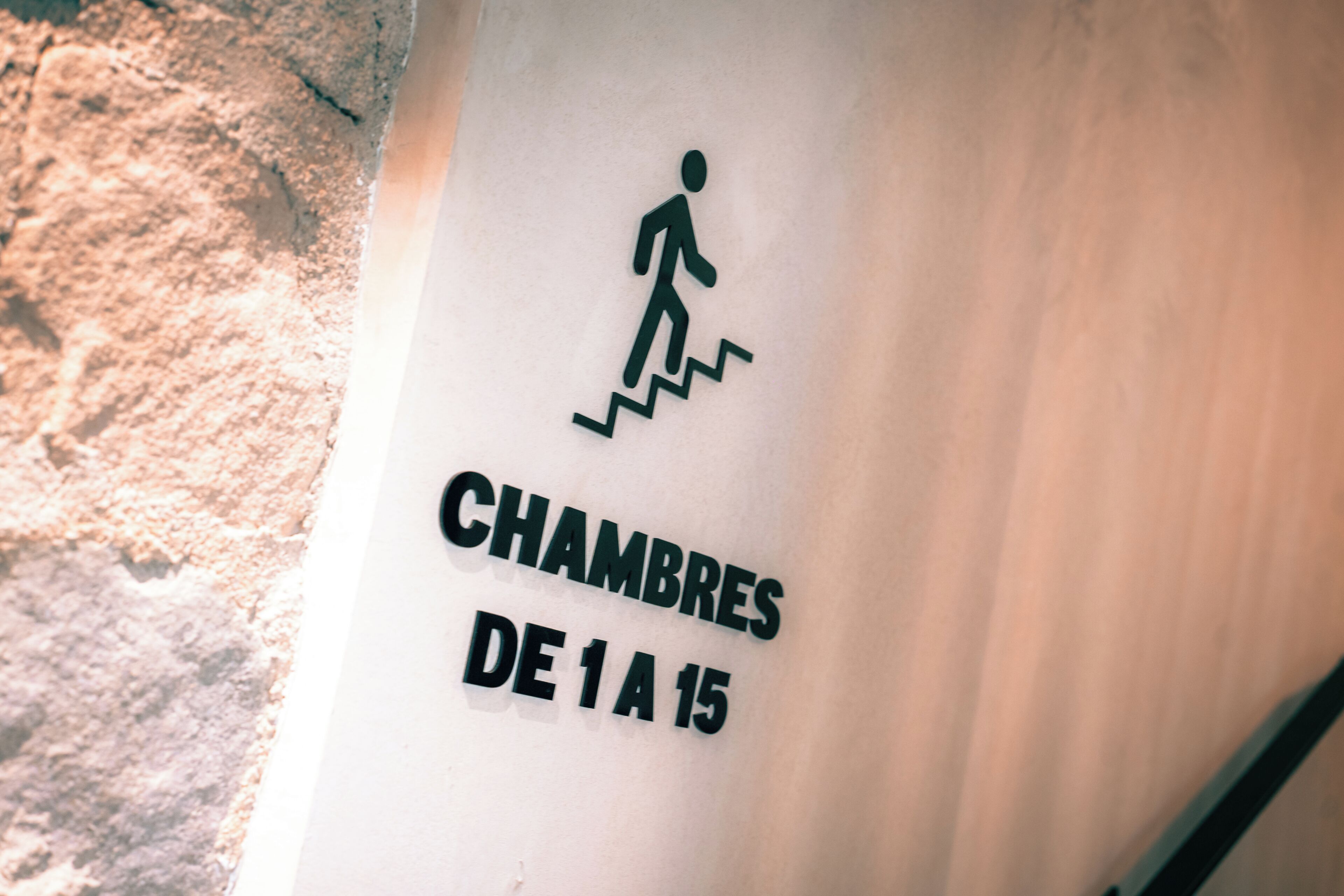 Pared con un símbolo de una persona escalando escaleras y texto que indica 'CHAMBRES DE 1 A 15', sugiriendo disponibilidad de habitaciones del 1 al 15.