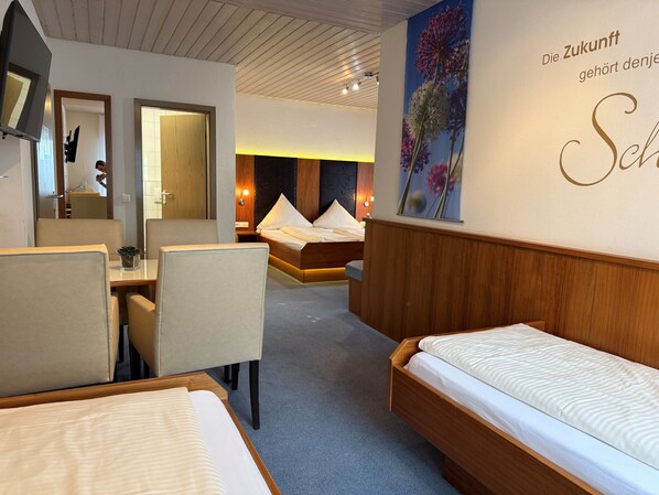 A hotel room with a bed, a desk, and a chair. There is a mirror and a wall with a floral painting.