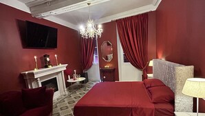 Ein Schlafzimmer mit einem großen Bett, einem Kamin, einer Kristallleuchtre und roten Vorhängen.