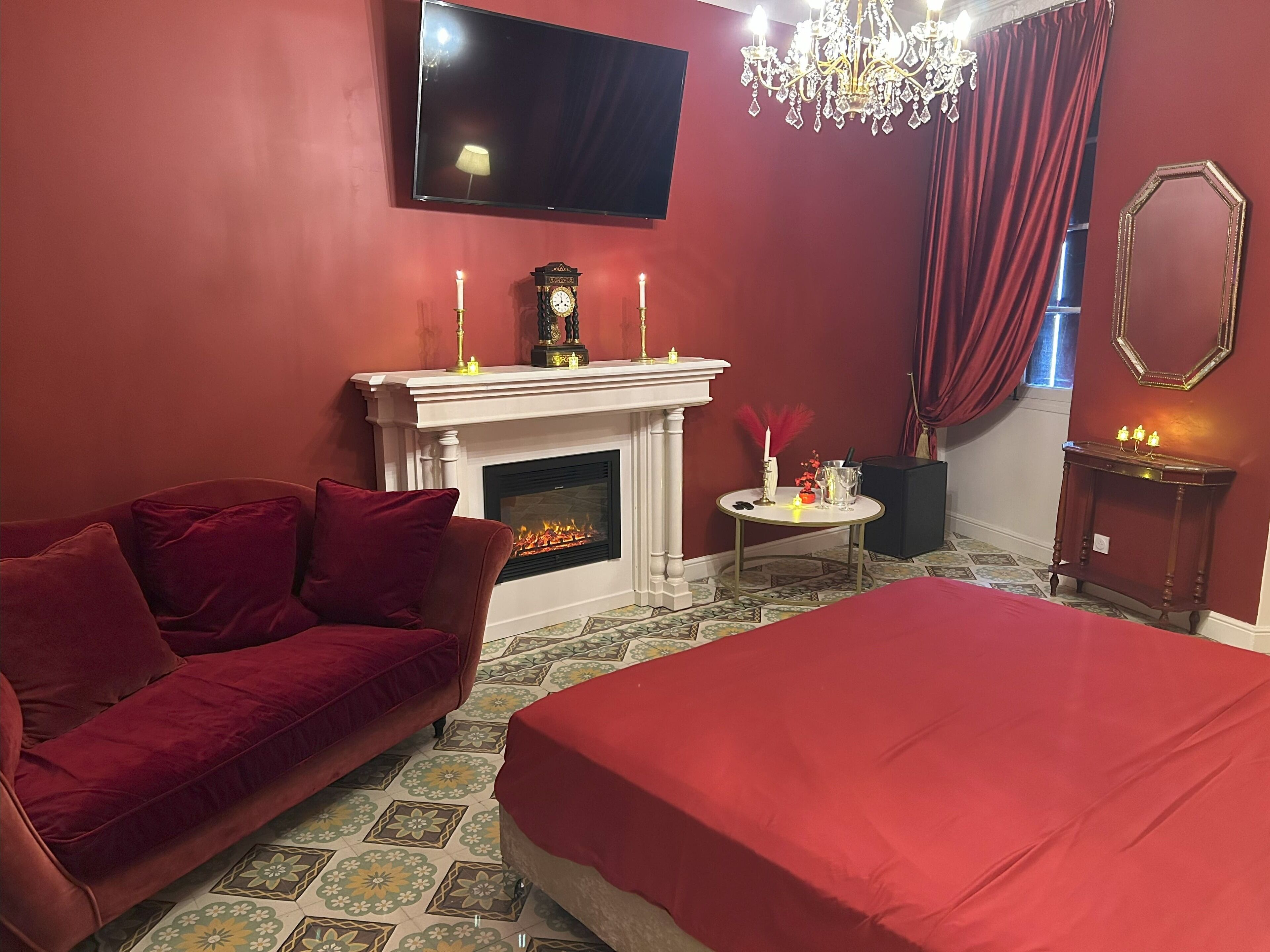 Una habitación con sofá rojo, cama, chimenea, televisión y candelabro.