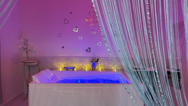 Ein modernes Badezimmer mit einer freistehenden Badewanne, einem kleinen Tischchen mit einer Vase und dekorativen Herzaufklebern an der Wand.