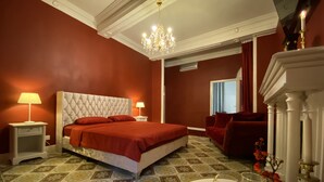 Ein Hotelzimmer mit einem großen Bett, einer Kristallleuchtre, einem roten Sessel, einem Kamin und einem gefliesten Boden.
