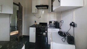 Une cuisine compacte avec des meubles blancs, une cuisinière noire et un four à micro-ondes. On y trouve un petit réfrigérateur et un grille-pain sur le plan de travail.