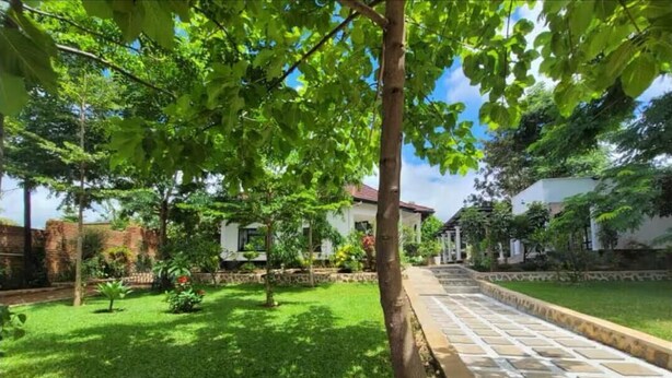 Un jardin bien entretenu, avec un chemin pavé menant à un bâtiment blanc surmonté d’un toit rouge.