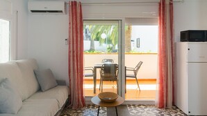 A living room with a sofa, a dining table with chairs, a refrigerator, and a sliding glass door leading to an outdoor area with a table and chairs. - WELCS APARTMENT 273 EMP with public swimming pool (Rosas / Roses)