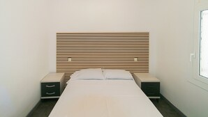 A minimalist bedroom with a wooden slat headboard, a single bed, two bedside tables with drawers, and a window on the right. - WELCS APARTMENT 273 EMP with public swimming pool (Rosas / Roses)