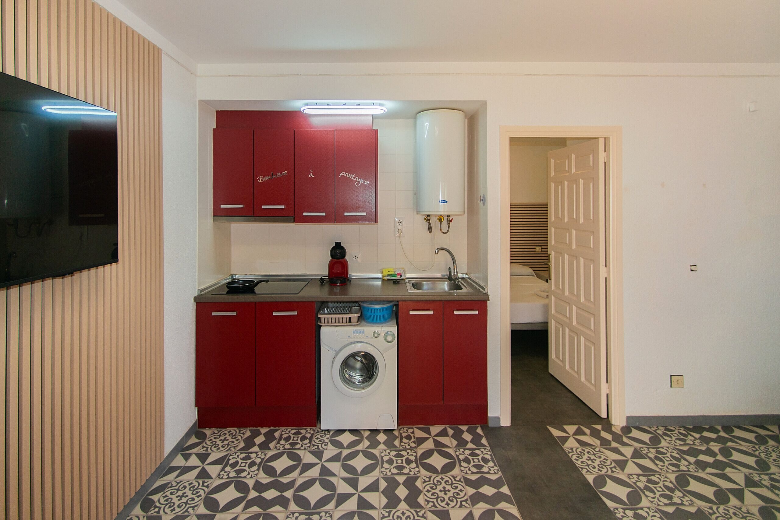 A compact kitchen with red cabinets, a washing machine, and a sink.