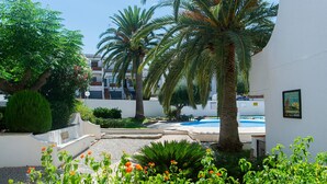 A courtyard with palm trees, a swimming pool, and a white building with a sign. - WELCS APARTMENT 273 EMP with public swimming pool (Rosas / Roses)