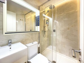 Ein modernes Badezimmer mit einer gläsernen Duschkabine, einem weißen Waschbecken und einer Toilette.
