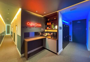 Eine moderne Hotelhalle mit einer Kaffeebar, einem neonbeleuchteten Schild mit der Aufschrift "Coffee Corner" und einem blauen Empfangsbereich.