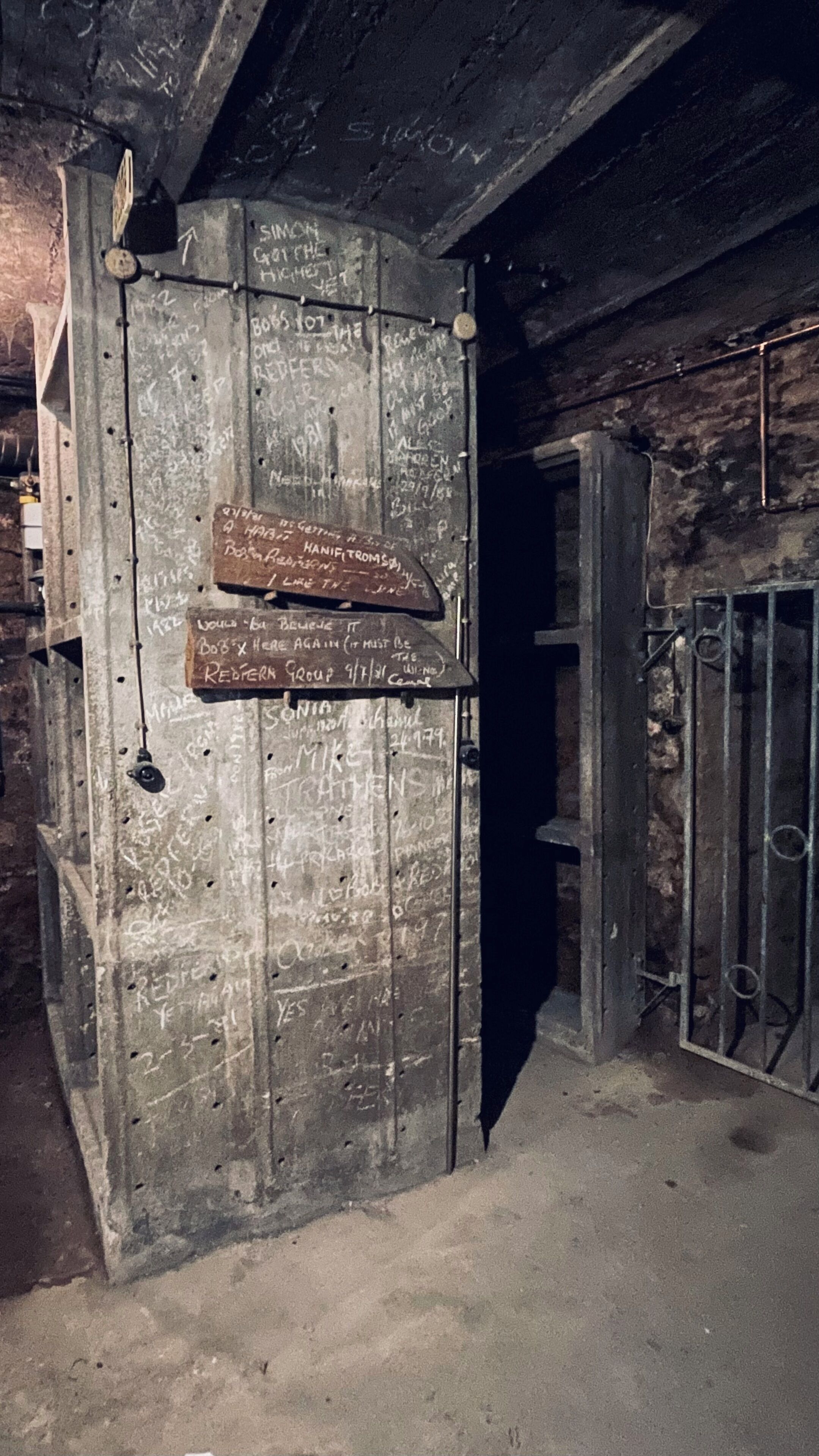Une porte en métal recouverte de graffitis et de notes manuscrites, un portail en métal et un mur en béton.