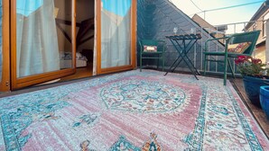 A room with a large sliding glass door leading to a balcony, a patterned rug, two green chairs, and a small table with glasses. - Former wine château (Winningen)