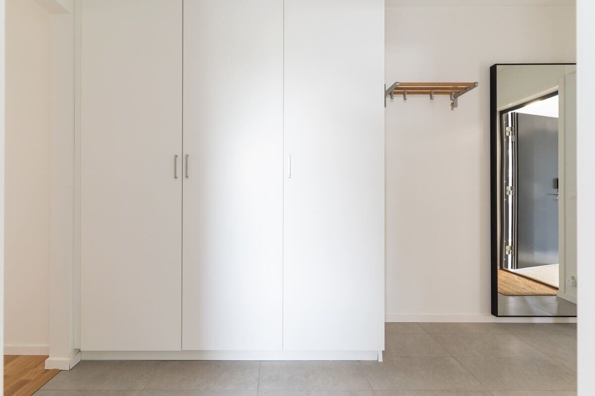 A room with a large white wardrobe, a wooden shelf, and a mirror on the wall.
