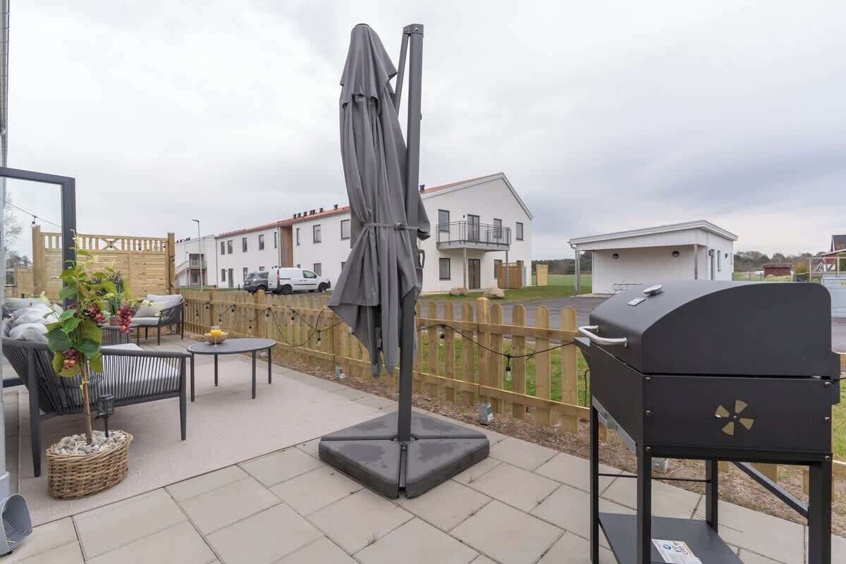 Une terrasse extérieure équipée d’un barbecue, d’un parasol et de meubles de jardin.