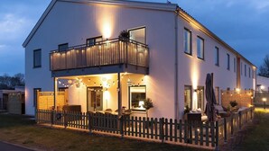 Una casa moderna de dos pisos con balcón, patio cercado y mobiliario exterior.